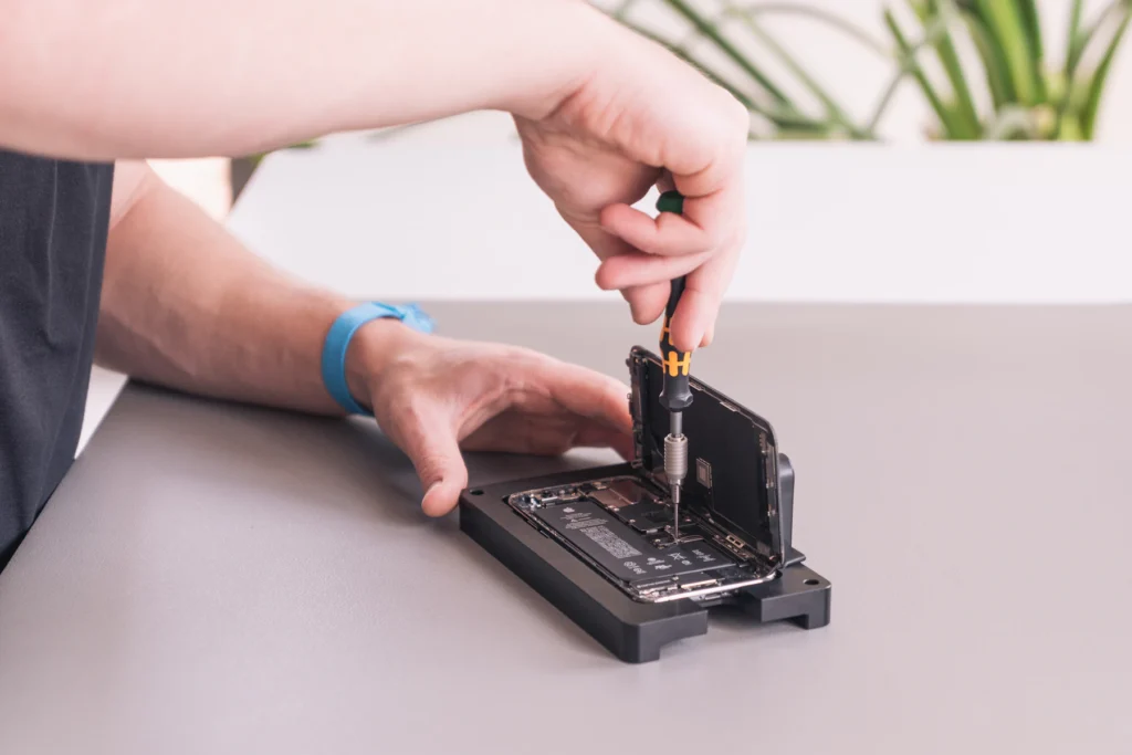 Mains d’un réparateur dévissant un smartphone maintenu sur un support